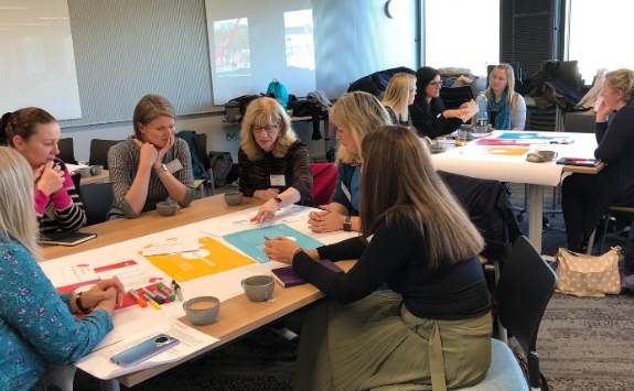 Groups of people sit around tables working collaboratively together